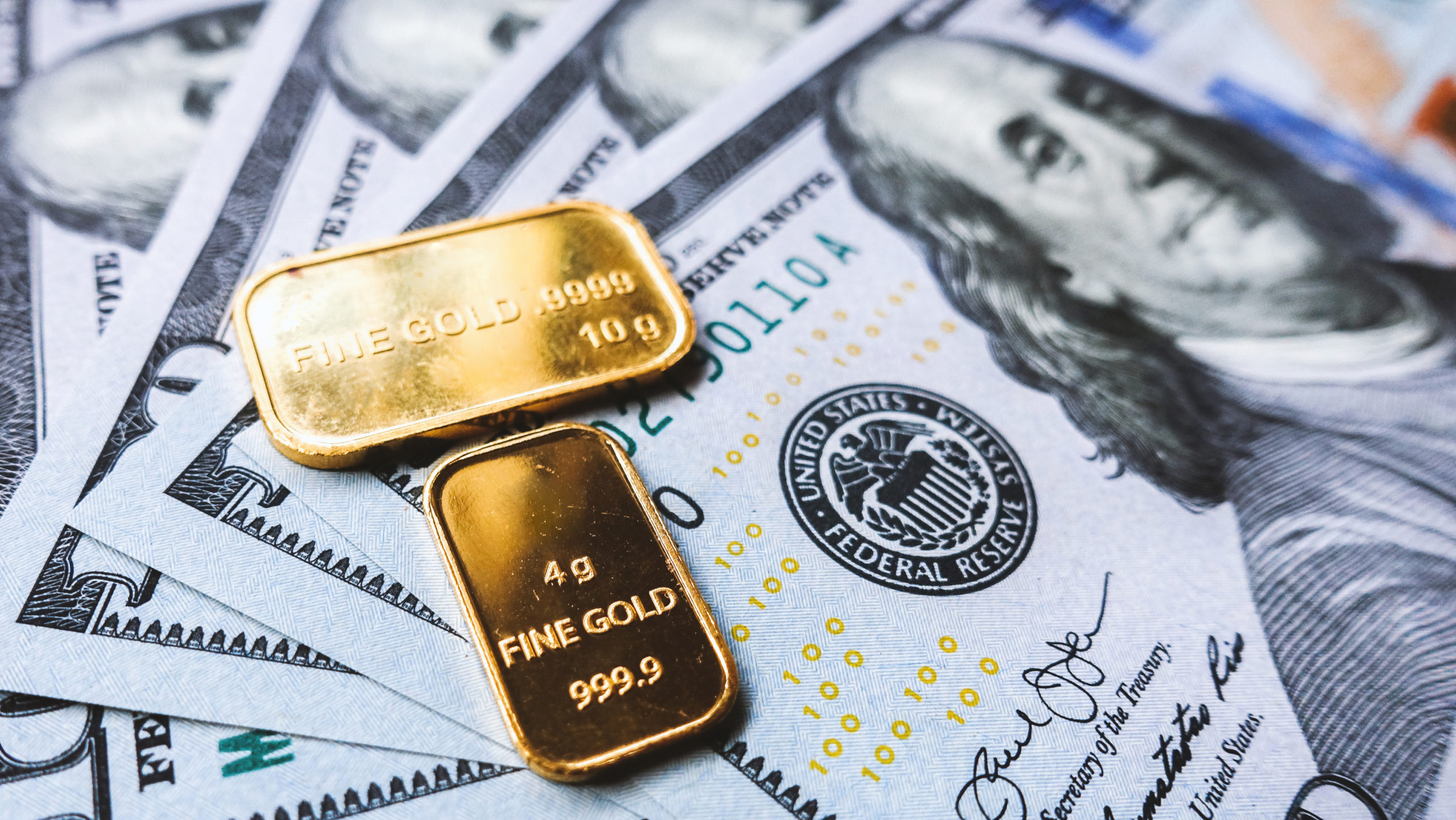 Pile of US dollar bills and gold plates amid Gold Remains Supported by The Recessionary Uncertainty